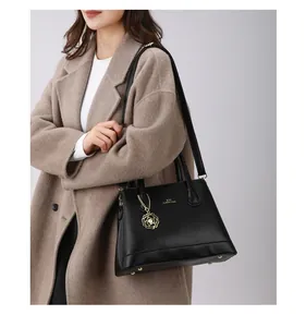 Detail of black pebbled leather tote bag with gold flower charm and removable shoulder strap
