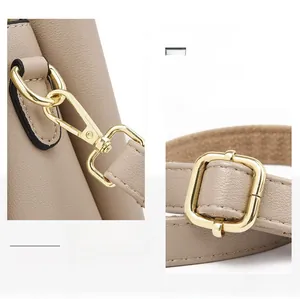 Detailed view of polished golden swivel hooks and buckles on beige textured leather bag