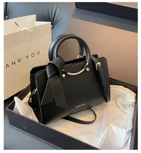 Detail of black PU leather handbag with gold lettering and decorative ribbon in gift box