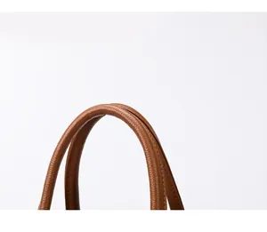Detail of caramel brown handbag handle with refined stitching and lychee leather texture
