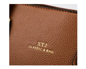 Close-up of brown pebbled leather texture with gold XTJ logo on large tote bag