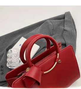 Detail of red bucket bag with curved handles, gold ring hardware and leather bow knot