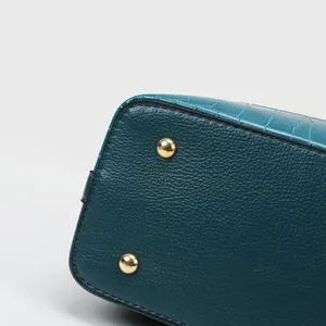 Dettaglio della borsa verde scuro con trama a grana, stampa coccodrillo e piedini dorati
