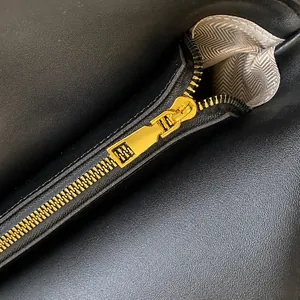 Detailed macro view of smooth gold zipper and textured black leather on shoulder bag