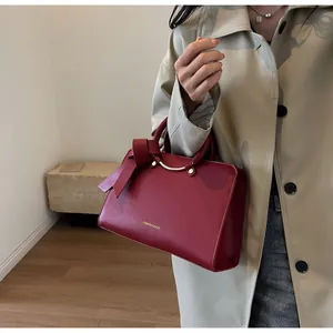 Detail of dark red bucket bag featuring metal handles and leather bow on beige coat