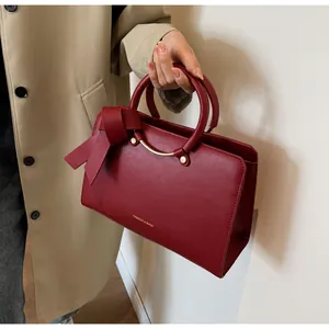 Detail of red faux leather bucket bag with structured round handles and ribbon bow