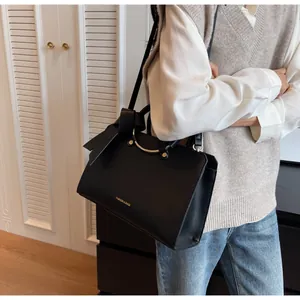 Detail of black leather crossbody bag with golden handle and side bow charm on model