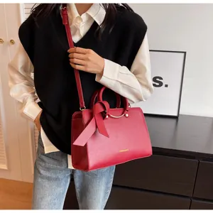 Detail view of red textured bucket bag with silk ribbon handle and golden fashion text