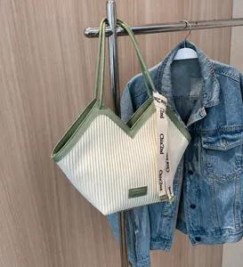 Detail of cream pleated tote bag featuring green V-neck trim and canvas letter ribbon
