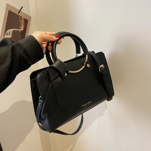 Black leather bucket bag with bow detail and gold handle shown as crossbody handbag