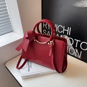 Red matte leather bucket bag with top handles and a large side bow on a white surface