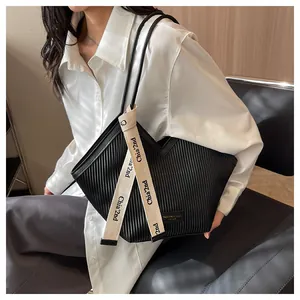 Close-up of black pleated tote bag featuring decorative cream woven strap and V-shaped cut