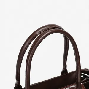 Detail of high-quality brown leather tote bag handles with precise stitching and texture