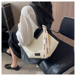 Detail of a pleated cream canvas tote bag with black trim and a decorative ribbon strap