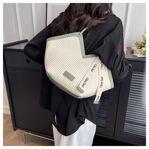 Detail of beige pleated canvas tote bag with green leather trim on a model shoulder