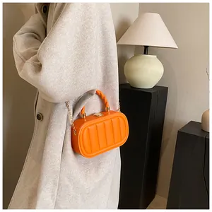 Detail of orange striped crossbody bag with golden chain and spiral handle on model