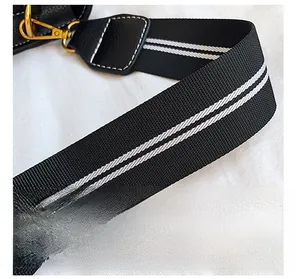 Detail of woven black and white striped bag strap with gold metal hooks and leather trim