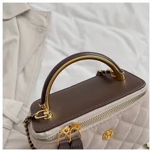 Detalle del bolso de ante acolchado con asa de anillo dorado y cierre floral de metal
