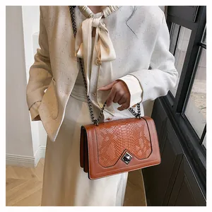 Détail d'un sac à bandoulière marron avec texture serpent et fermoir rotatif argenté