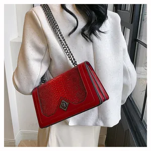 Gros plan d'un sac rouge à texture serpent avec chaîne en métal et fermoir pivotant chic