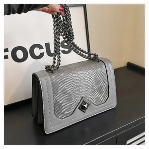Détail du sac gris avec gaufrage serpent, chaîne en métal noir et fermoir rotatif