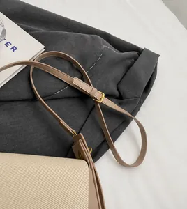 Detail of adjustable leather strap and golden buckle on beige canvas crossbody bag