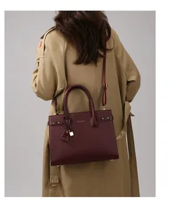 Dettaglio della borsa in pelle bordeaux con chiusura dorata e logo mostrata dalla modella