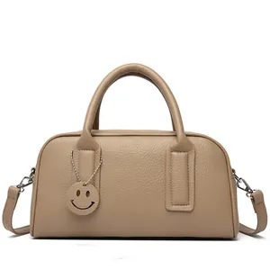 Detail view of khaki pebbled leather Boston bag with a round smiley face charm