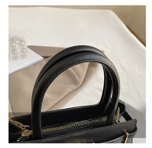 Detail of black leather handbag featuring round handles and premium gold metal zippers