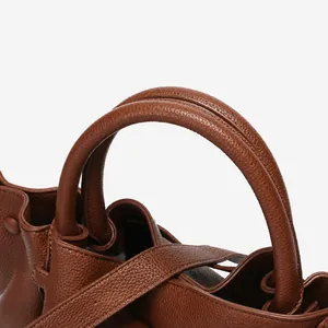 Close-up of pebble leather texture and sturdy handle stitching on brown tote bag