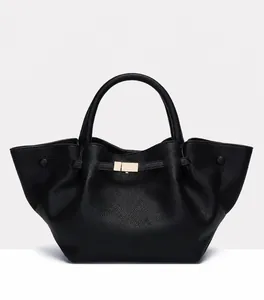 Detail of black tote bag with lychee texture and gold buckle on a light grey background