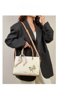 Détail de la broderie florale dorée sur un sac à main vintage en cuir blanc texturé