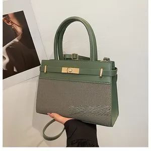 Detail of dark green tote bag featuring leather stitching and gold metal lock buckle