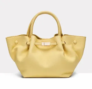 Detail of light yellow leather tote bag featuring metal snap fastener and litchi texture