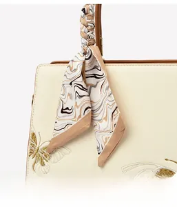 Détail de broderie papillon dorée et foulard en soie sur un sac fourre-tout beige