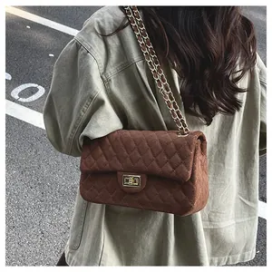 Detail view of a quilted brown velvet crossbody bag with golden chain on a model