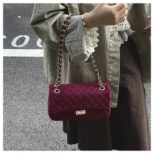Detail of burgundy velvet quilted bag with golden chain strap and metallic lock closure