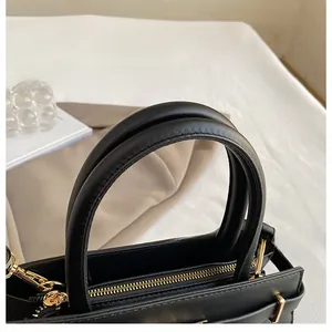 Detail of round handles and gold hardware on a black textured leather handbag