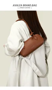 Borsa baguette marrone in pelle grana litchi indossata da una modella su cappotto