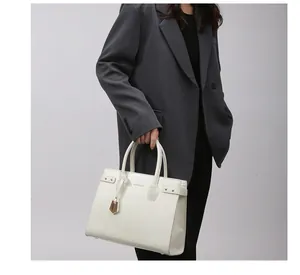 Detail of ivory faux leather tote bag with gold lettering and metallic charm accessory