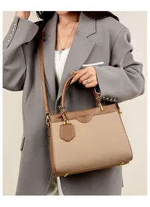 Detail einer beigen Canvas-Handtasche mit braunem Lederbesatz und Goldbeschlägen