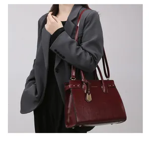 Detail of burgundy tote bag with gold hardware and removable shoulder strap worn by a model