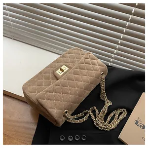 Detail of brown quilted velvet bag with gold rectangular lock and metal chain strap