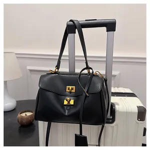 Close-up of black leather tote bag with gold swivel lock hanging on white luggage