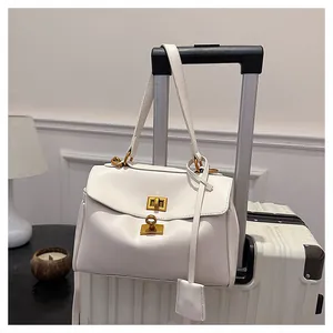 White leather tote bag detail with golden twist lock hanging on a white suitcase