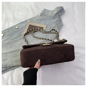 Detail of coffee brown velvet quilted bag with gold chain strap on denim jacket