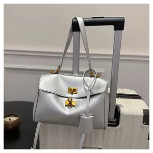 Detail view of silver tote bag featuring gold turn-lock closure on white luggage