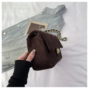 Detail of dark brown quilted velvet bag with gold chain strap and metal lock closure