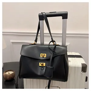 Detail of black leather tote bag with double gold turn-lock closure on white suitcase