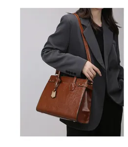 Close-up of brown glossy leather handbag with gold rivets and adjustable strap details